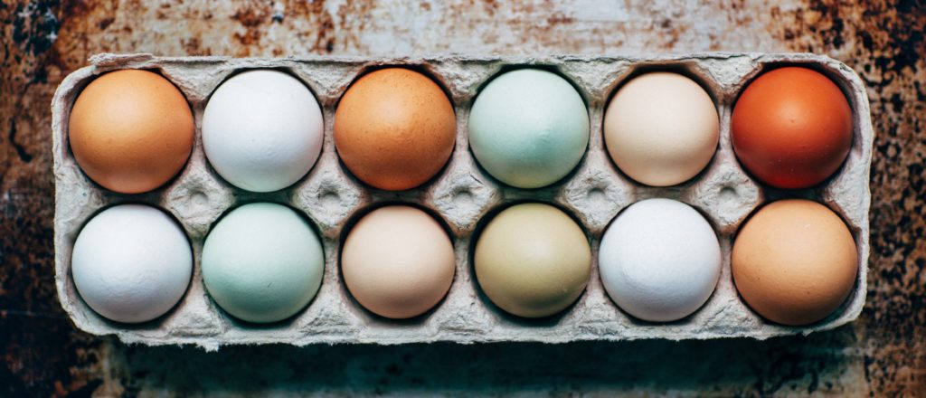 A carton of a dozen eggs in various shades of white and brown.
