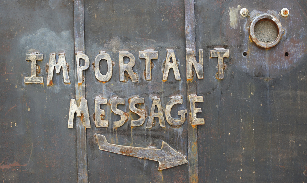 Un letrero en una puerta metálica dice “Mensaje Importante” con una flecha apuntando a la derecha.