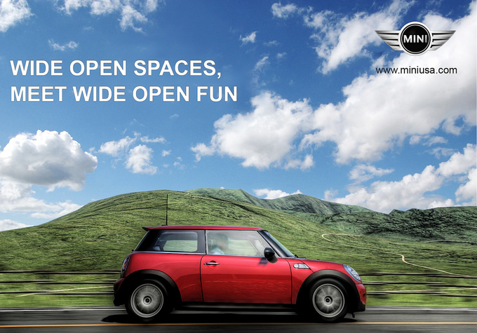A Mini car drives down a road on a beautiful sunny day by some scenic hills. Text says "Wide Open Spaces, Meet Wide Open Fun."
